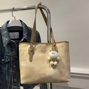 Detail of beige suede tote bag with gold logo lettering and a plush keychain