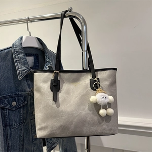 Large gray tote bag with black handles and white fluffy cloud charm on denim background