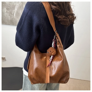 Detail of soft brown leather hobo bag with teddy bear charm and woven tassel accessory