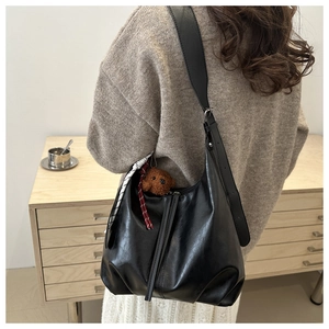 Detail of a black crescent shoulder bag with teddy pendant and striped scarf on model