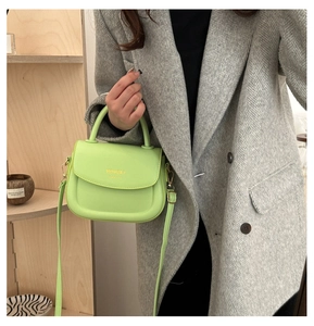 Gros plan du sac de selle en cuir vert vif avec lettrage doré porté sur un blazer