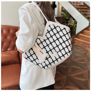 Detail of black and white checkered tweed tote bag featuring white leather handles and ribbon
