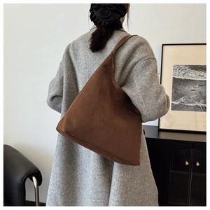 Brown suede tote bag with wide strap worn by model in a minimalist home setting