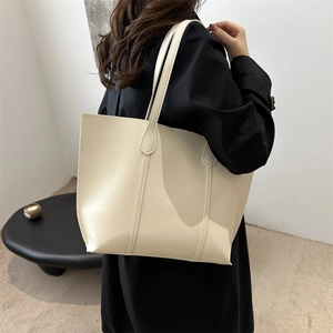 Grand sac fourre-tout minimaliste blanc crème porté par un mannequin en manteau sombre