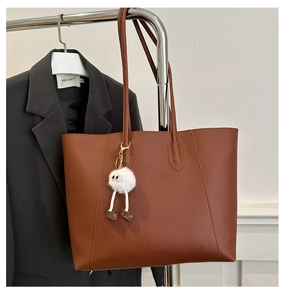 Detail of a brown lychee pattern leather tote bag with a quirky white fur monster charm