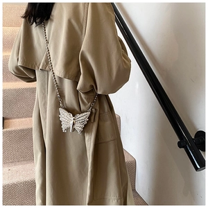 Detail of silver butterfly crossbody bag with rhinestones on a stylish beige trench coat
