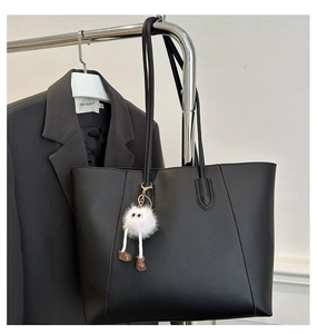 Detail view of large black matte tote bag featuring a cute white plush monster charm