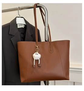 Detail of brown faux leather tote bag with white plush monster charm on a metal hanger