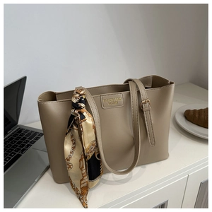Detail of beige leather tote bag with gold logo plate and silk scarf on a work desk