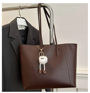 Close-up of a brown leather tote bag featuring a cute white plush monster charm