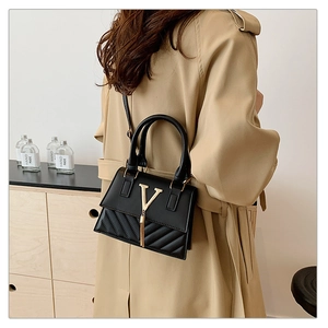 Detail of a black leather crossbody bag with gold V-buckle and tassel on a khaki coat