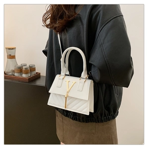 Detail of white quilted handbag featuring gold V-buckle, fringe tassel and leather strap