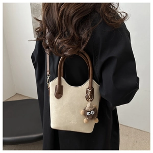 Detail of beige bucket bag with dark brown handles and cute monster plush charm accessory