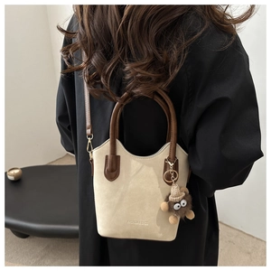 Fashionable crossbody bucket bag in beige leather with brown strap and plush charm