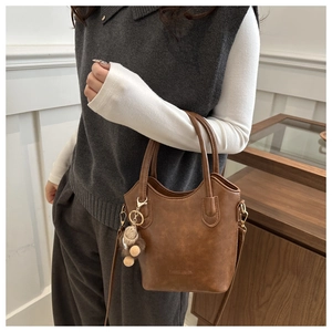 Detail of a brown leather bucket bag featuring a plush bear charm and long shoulder strap