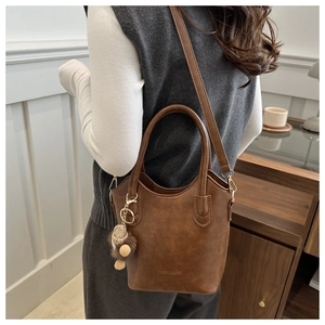 Detail of dark brown bucket bag with plush charm shown worn by a model in a casual setting