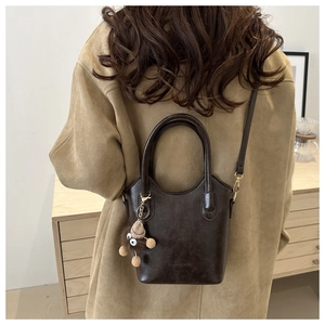 Detail of dark brown leather bucket bag with a cute plush charm on a camel wool coat