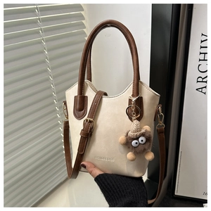 Detail of beige bucket bag with contrast brown trim and cute monster plush pendant
