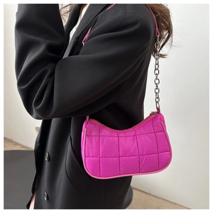 Dettaglio della borsa a mezzaluna fucsia trapuntata con catena argento su blazer nero