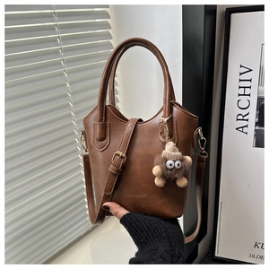 Detail of a brown leather bucket bag featuring a plush monster charm and embossed logo