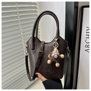Detail of coffee leather bucket bag with plush charm and adjustable shoulder strap