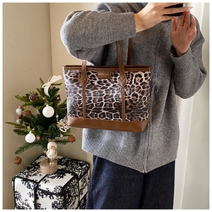 Detail of leopard print tote bag with brown leather handles and brand logo tag