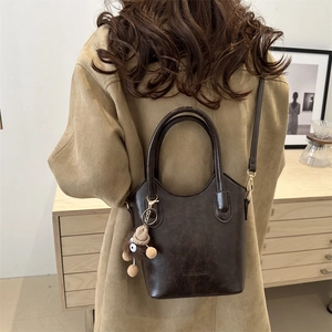 Dark brown bucket bag with plush bear charm shown in a minimalist home setting