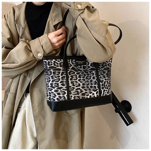 Detailed close-up of leopard print tote bag with black leather trim and logo patch