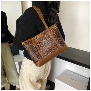 Detail view of large leopard print tote bag with brown leather handles worn by a model