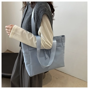 Detail of light blue nylon tote bag with wide strap and side pocket on a model