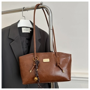 Detail of dark brown leather tote bag featuring a gold bell pendant and logo plate
