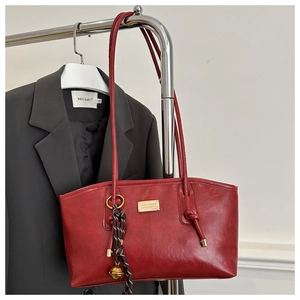 Close-up of red leather tote bag featuring gold logo plate and decorative woven tassel knot