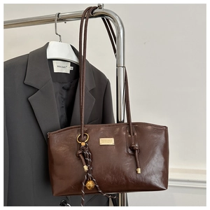 Detail of dark brown vintage faux leather tote with metallic logo and woven pendant