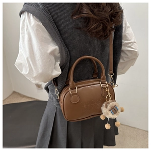 Detail of a brown Boston style crossbody bag with an embossed logo and sheep plush charm