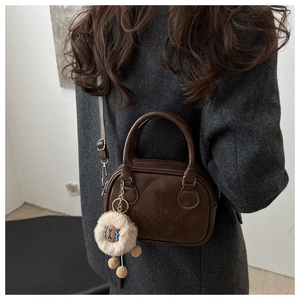 Detail einer braunen Lederhandtasche mit Lucky Ohio Prägung und Plüsch-Anhänger