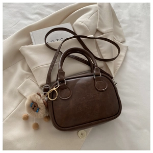Detailansicht der dunkelbraunen Vintage-Tasche mit Prägung und süßem Bären-Anhänger
