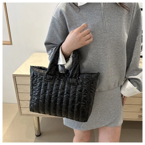 Detail of a black quilted puffer tote bag showing padded nylon texture and shoulder carry