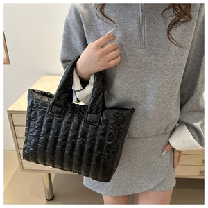 Detail of a black quilted puffer tote bag with glossy finish held by a model
