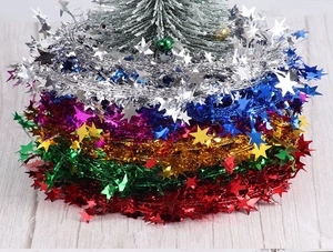 Close-up of shiny star tinsel garlands in assorted colors around a white Christmas tree