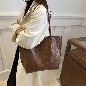 Brown woven tote bag in classic Intrecciato style shown on model with shoulder strap