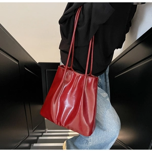 Detailed view of large bright red high-gloss tote bag with soft leather texture and pleats