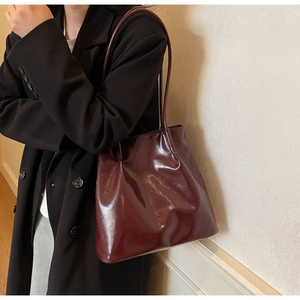 Close-up of a burgundy vintage tote bag in glossy leather on a black suit shoulder