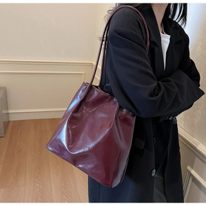 Side view of model wearing a large burgundy glossy leather tote bag with pleated detail