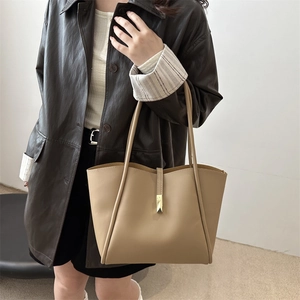 Chic khaki tote bag with gold metal hardware carried by a model in a leather jacket