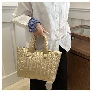 Detail of a gold quilted tote bag with a metallic finish and soft padded top handles