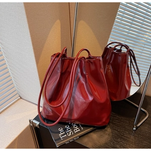 Detail of burgundy glossy leather tote bag with soft folds on a vintage book backdrop