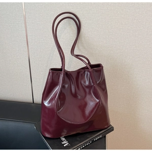 Detailed view of glossy burgundy leather tote bag with soft texture on a book