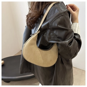 Close-up of a beige crescent suede shoulder bag worn with a dark leather jacket
