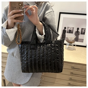Detail of a black quilted puffer tote bag with glossy nylon finish and padded handles
