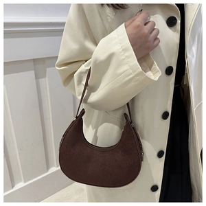Detail of a brown suede half-moon shoulder bag styled with a stylish beige trench coat
